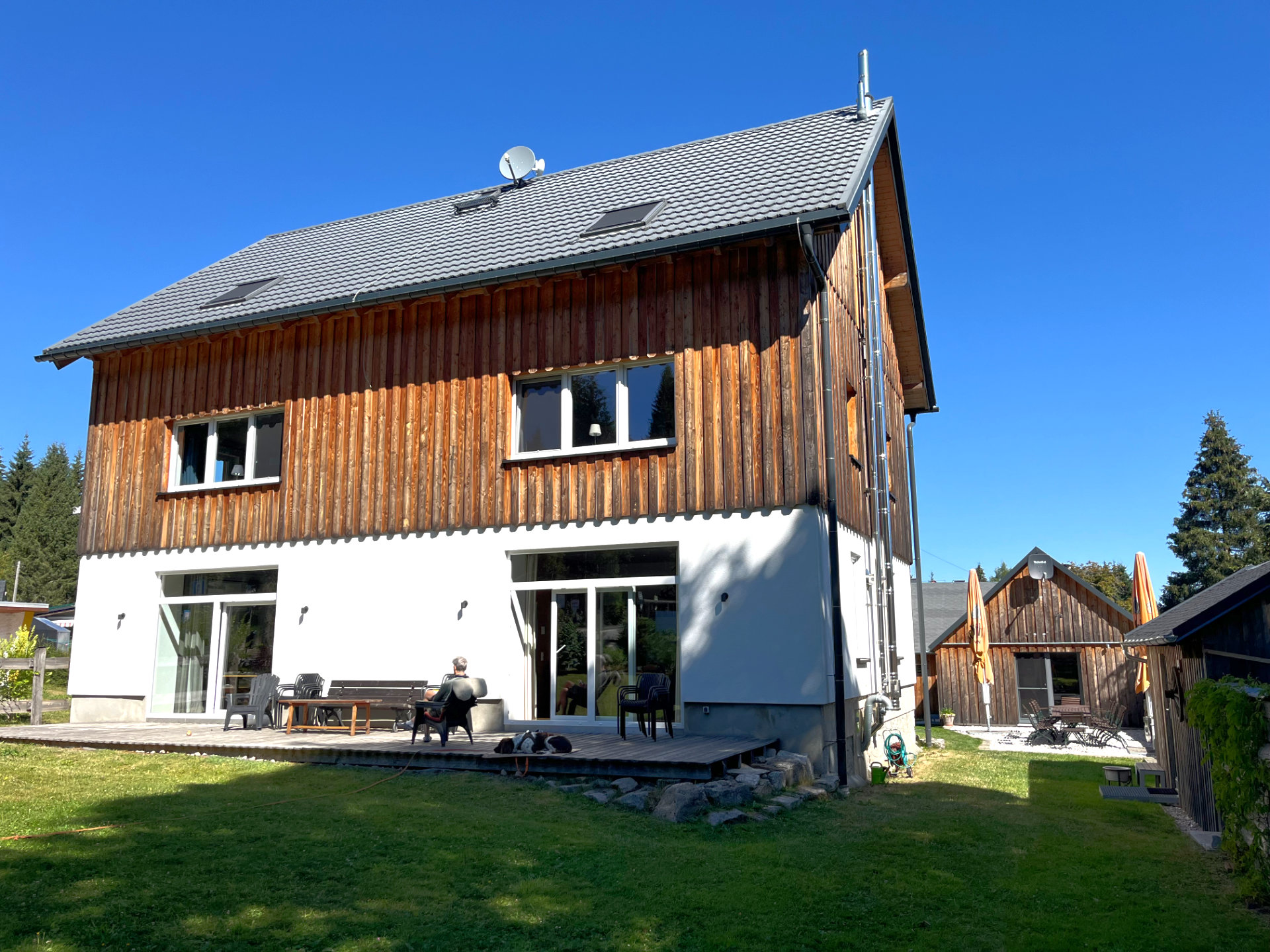 Eine Person sitzt in der Sonne auf der Terrasse vor der Berghütte Zum Kranichsee.