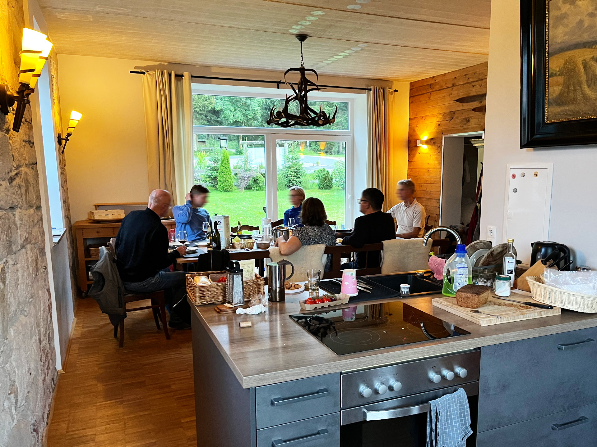 Blick über die Küchenzeile in den Gemeinschaftsraum Blick über die Küchenzeile in den Gemeinschaftsraum, Familie und Freunde sitzen beim Essen in der Berghütte Zum Kranichsee